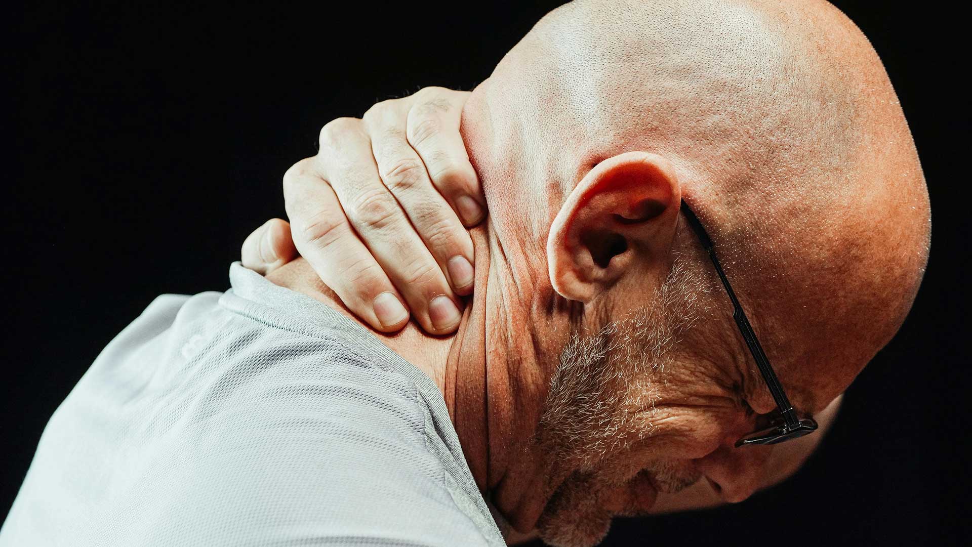 A man grimacing, holding the back of his neck